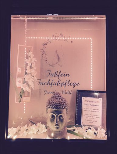 Buddha-Kopf mit Blumen und einem Schild für eine Fußpflegepraxis.