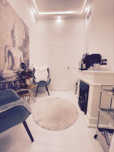 Heller Raum mit Buddha-Wandbild, bequemen Stühlen und einer Kaffeemaschine.