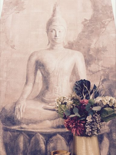 Buddha-Statue im Hintergrund mit einem Blumenarrangement im Vordergrund.