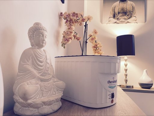 Buddhistische Statue neben einem weißem Gefäß mit Blumen und einer Lampe im Hintergrund.