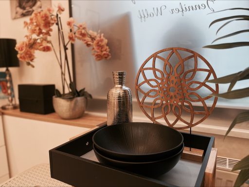 Schwarze Schalen auf einem Tablett mit einer dekorativen Blüte im Hintergrund.